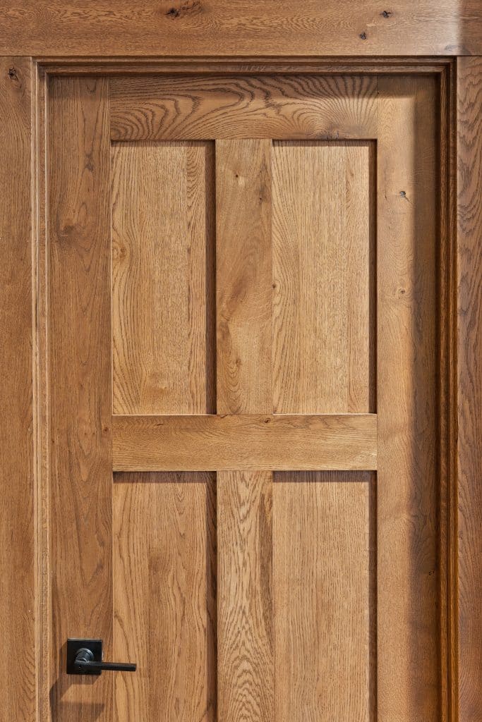 A wooden door with a natural finish and rustic wood appeal, featuring a simple rectangular panel design and a modern black handle on the left side.